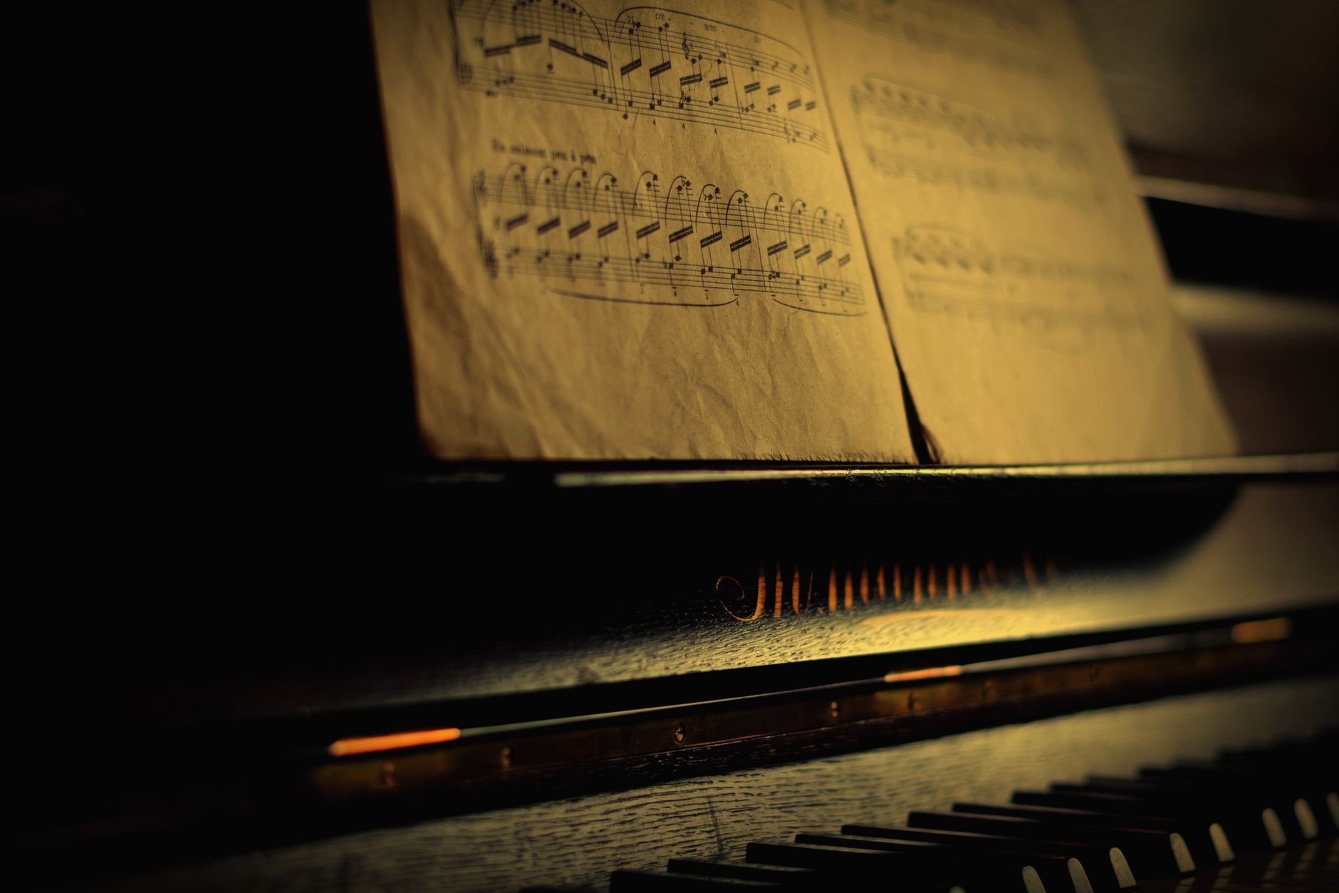 Close-up of vintage piano keys and music sheet with warm, moody lighting.