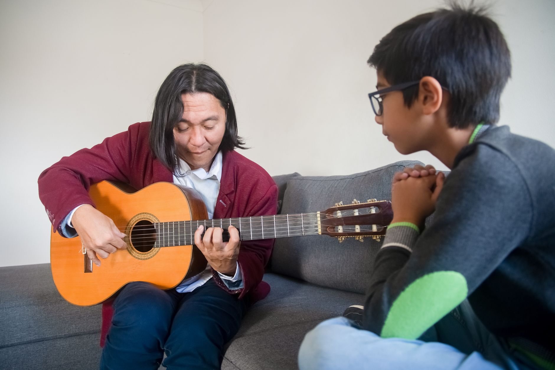 Acoustic guitar lesson with a teacher instructing a young student in a cozy indoor setting.