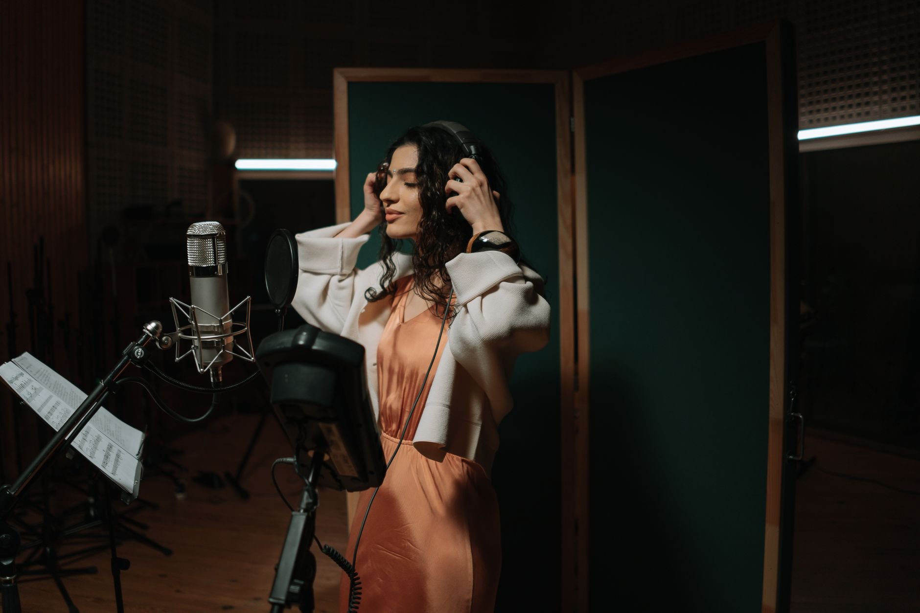Female singer recording music in a professional studio wearing headphones and using a microphone.